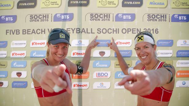 Zwei Beachvolleyballspielerinnen zeigen auf den Betrachter vor einer Sponsorenwand des FIVB Beach Volleyball Sochi Open 2016.