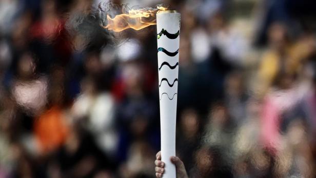 Eine Hand hält eine olympische Fackel vor einer Menschenmenge.