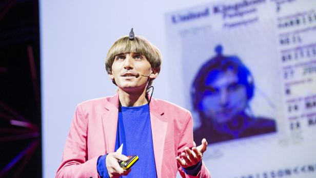 Ein Mann mit einem Sensor auf dem Kopf hält eine Präsentation vor einem Reisepass-Foto.