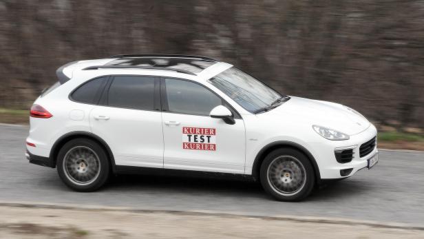 Ein weißer Porsche Cayenne mit „Kurier Test Kurier“-Aufklebern fährt auf einer Straße.