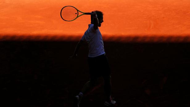 Ein Tennisspieler schlägt den Ball vor einem orangefarbenen Himmel.