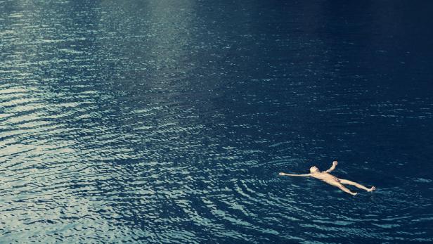 Eine Person treibt entspannt auf dem dunklen Wasser.