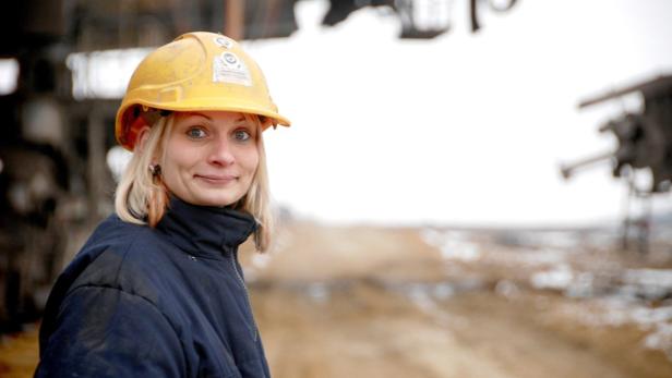 Eine Frau mit gelbem Schutzhelm blickt in die Kamera.