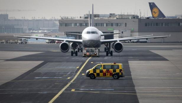 Ein Flugzeug wird auf dem Rollfeld von einem Schlepper gezogen, während ein gelbes Begleitfahrzeug daneben steht.