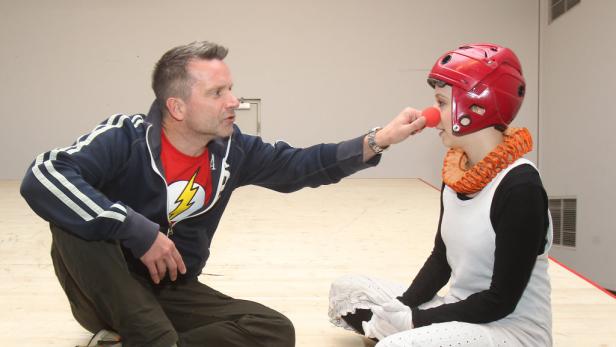 Ein Mann setzt einer Person mit rotem Helm und Clownsnase eine rote Nase auf.