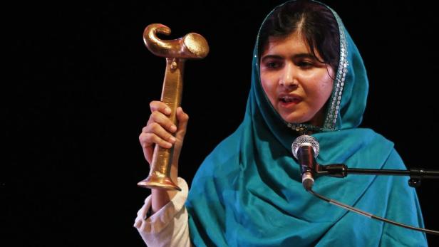 Malala Yousafzai hält eine goldene Statue in der Hand und spricht in ein Mikrofon.