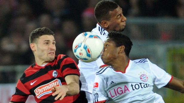 Drei Fußballspieler kämpfen um den Ball während eines Spiels.