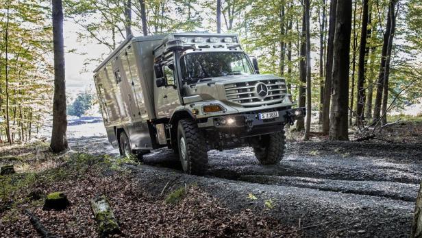 Ein Mercedes-Benz Unimog Expeditionsmobil fährt durch einen Wald.