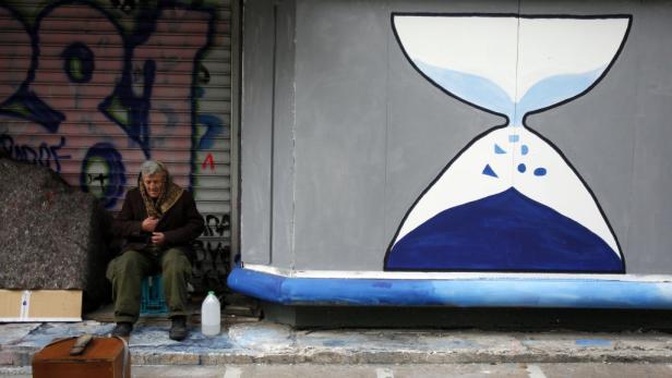 Eine ältere Frau sitzt vor einer Wand mit Graffiti und einer aufgemalten Sanduhr.