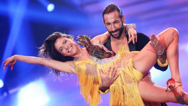 Ein Mann hält eine lächelnde Frau in einem gelben Kleid beim Tanzen hoch.