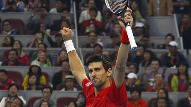 Novak Đoković feiert mit erhobenen Armen und Tennisschläger vor einer Zuschauermenge.