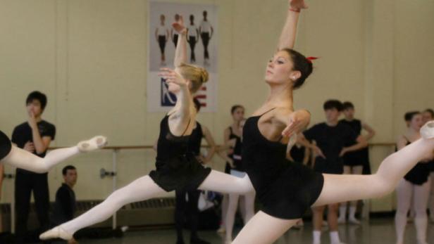 Mehrere Balletttänzerinnen in schwarzen Trikots springen während einer Probe.