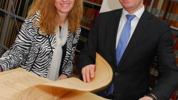 Zwei Personen betrachten ein großes, altes Buch in einem Archiv.