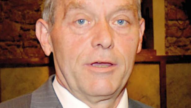 Ein Mann mit hellblauen Augen und Anzug mit Krawatte blickt in die Kamera.