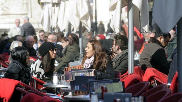 Menschen sitzen an Tischen in einem belebten Straßencafé.