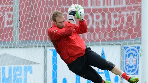 Ein Torwart in roter Jacke fängt einen Ball vor einem Tornetz.