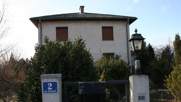 Ein zweistöckiges Haus mit Rollläden und einem Schild mit der Aufschrift „2 Am Bahnhof“.