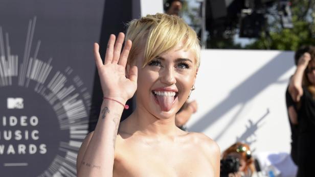 Miley Cyrus auf dem roten Teppich der MTV Video Music Awards, die Zunge herausstreckend.