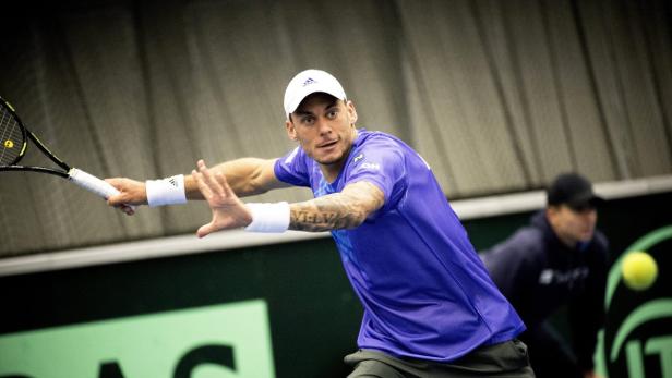 Ein Tennisspieler in blauer Sportkleidung schlägt einen Ball.