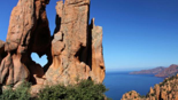 Eine Felsformation mit einem herzförmigen Loch vor dem Hintergrund des Meeres.