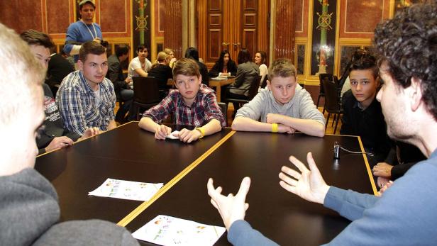 Eine Gruppe Jugendlicher sitzt an einem Tisch und hört aufmerksam zu.