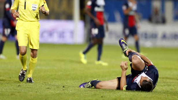 Ein Fußballspieler liegt verletzt auf dem Rasen, während ein Schiedsrichter auf ihn zuläuft.