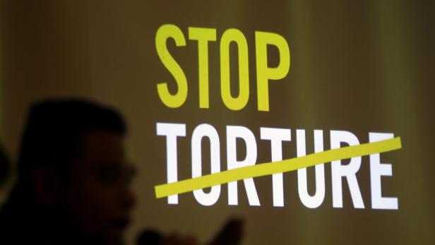 Der Schriftzug „Stop Torture“ ist mit einem gelben Strich durchgestrichen.