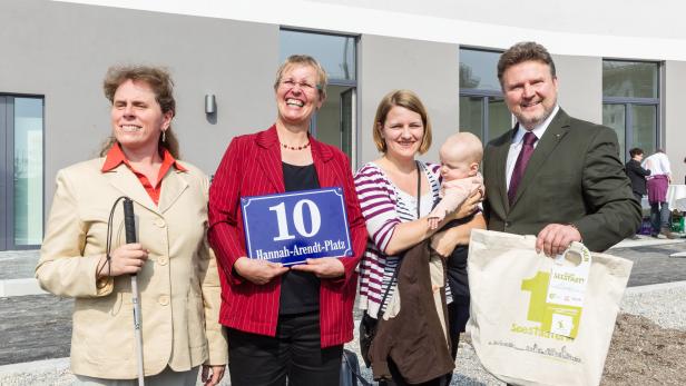 Eine Gruppe von Personen steht vor einem Gebäude mit einem Schild „Hannah-Arendt-Platz 10“.