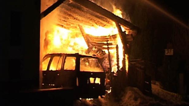 Ein Auto steht in einem brennenden Carport.