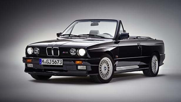 Ein schwarzes BMW E30 M3 Cabriolet vor einem grauen Hintergrund.