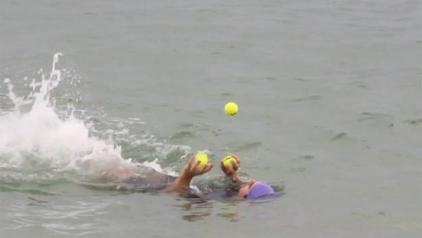 Eine Person schwimmt im Meer und jongliert mit Tennisbällen.