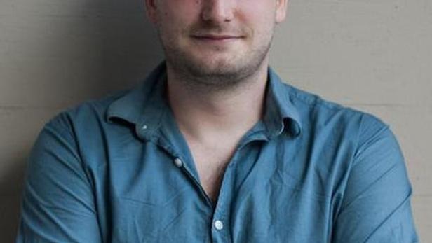 Ein Mann mit blauem Hemd und verschränkten Armen lächelt in die Kamera.