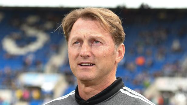 Ein Mann mit blonden Haaren und grauem Shirt vor einer blauen Zuschauertribüne.