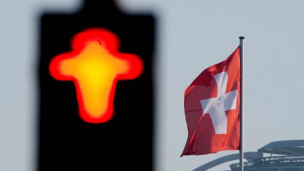 Eine Schweizer Flagge weht im Wind neben einem beleuchteten Kreuz.