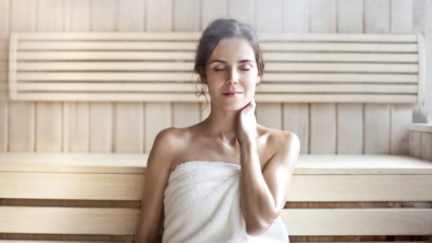 Eine Frau entspannt eingewickelt in ein Handtuch in einer Sauna.