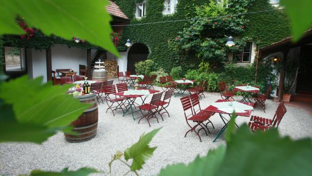 Ein idyllischer Innenhof mit Tischen und Stühlen vor einem mit Efeu bewachsenen Gebäude.