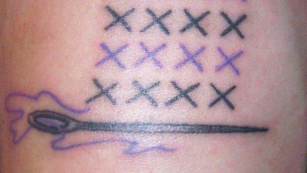 Ein Tattoo mit Kreuzstich-Motiven und einer Nadel mit Faden.