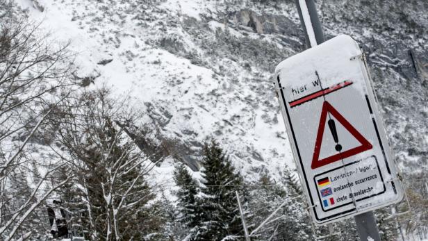 Ein Lawinengefahr-Schild steht vor einer verschneiten Berglandschaft.