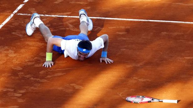 Ein Tennisspieler liegt erschöpft auf dem Sandplatz, sein Schläger liegt daneben.