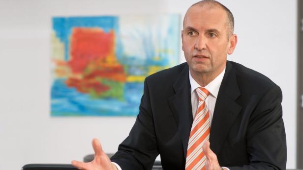 Ein Mann im Anzug gestikuliert vor einem abstrakten Gemälde.