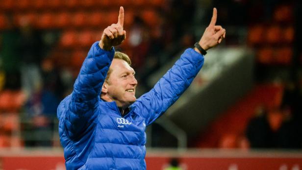 Ein Mann in einer blauen Jacke jubelt mit erhobenen Zeigefingern.