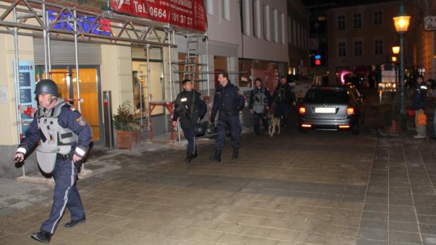 Polizisten mit Schutzwesten und einem Hund patrouillieren auf einer Straße.