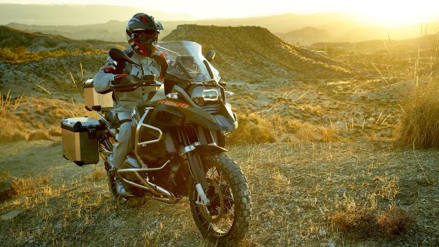 Ein Motorradfahrer auf einer BMW R1200 GS vor einer Hügellandschaft im goldenen Licht.