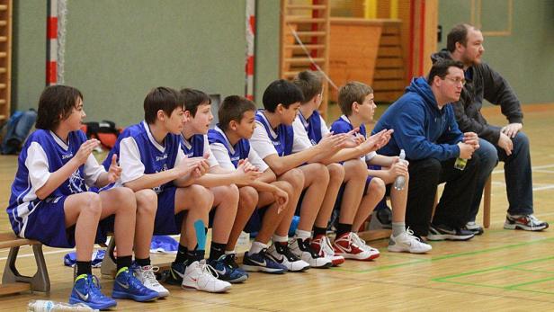 Eine Gruppe junger Basketballspieler sitzt mit ihren Trainern auf der Bank.