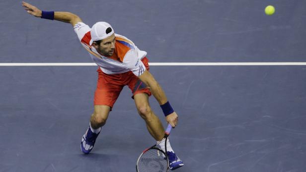 Ein Tennisspieler schlägt einen Ball auf einem blauen Platz.