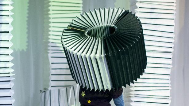 Eine Person trägt einen großen, runden Lampenschirm auf dem Kopf.