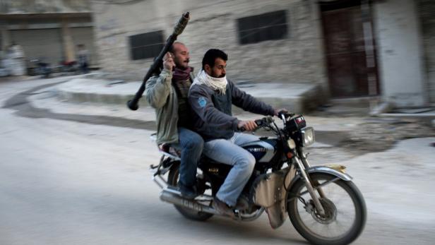 Zwei Männer fahren mit einem Gewehr auf einem Motorrad durch eine Stadt.