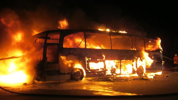 Ein Bus steht in Flammen, während ein Feuerwehrmann im Hintergrund steht.
