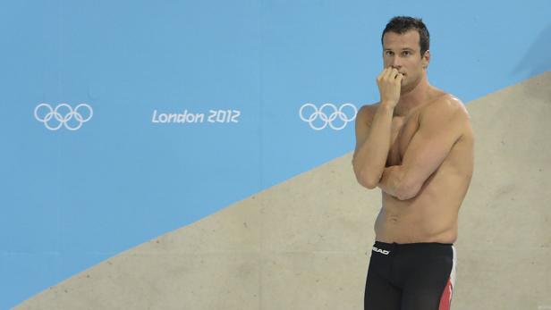 Ein Schwimmer steht vor einer Wand mit dem Logo der Olympischen Spiele 2012 in London.