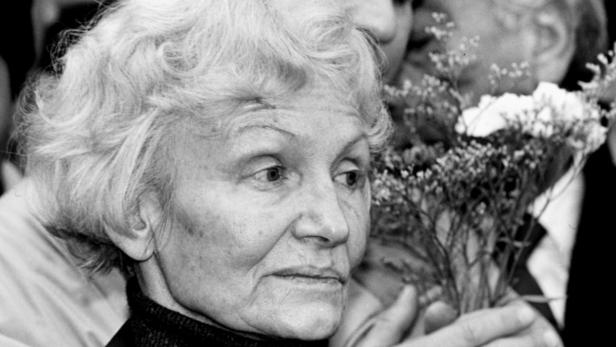 Eine ältere Frau mit lockigem Haar hält einen Blumenstrauß.